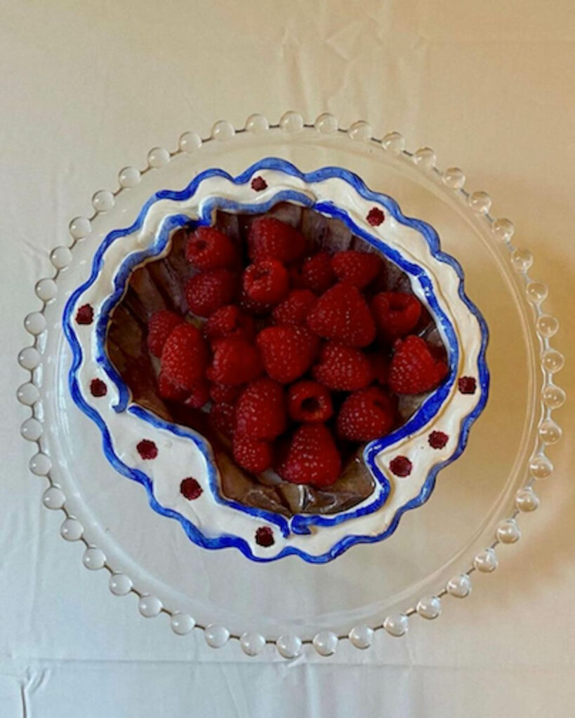 raspberries in a white ceramic bowl with blue trim and red dots on the lip