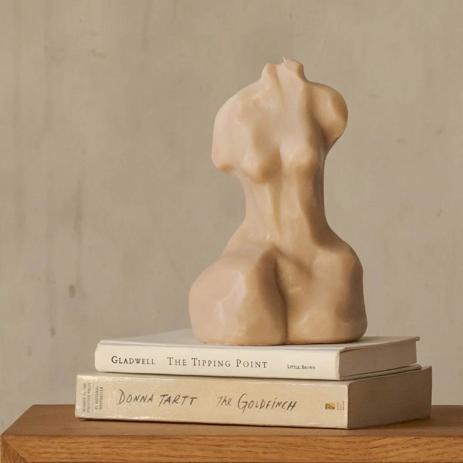 a candle in the shape of a woman's body atop a couple of books