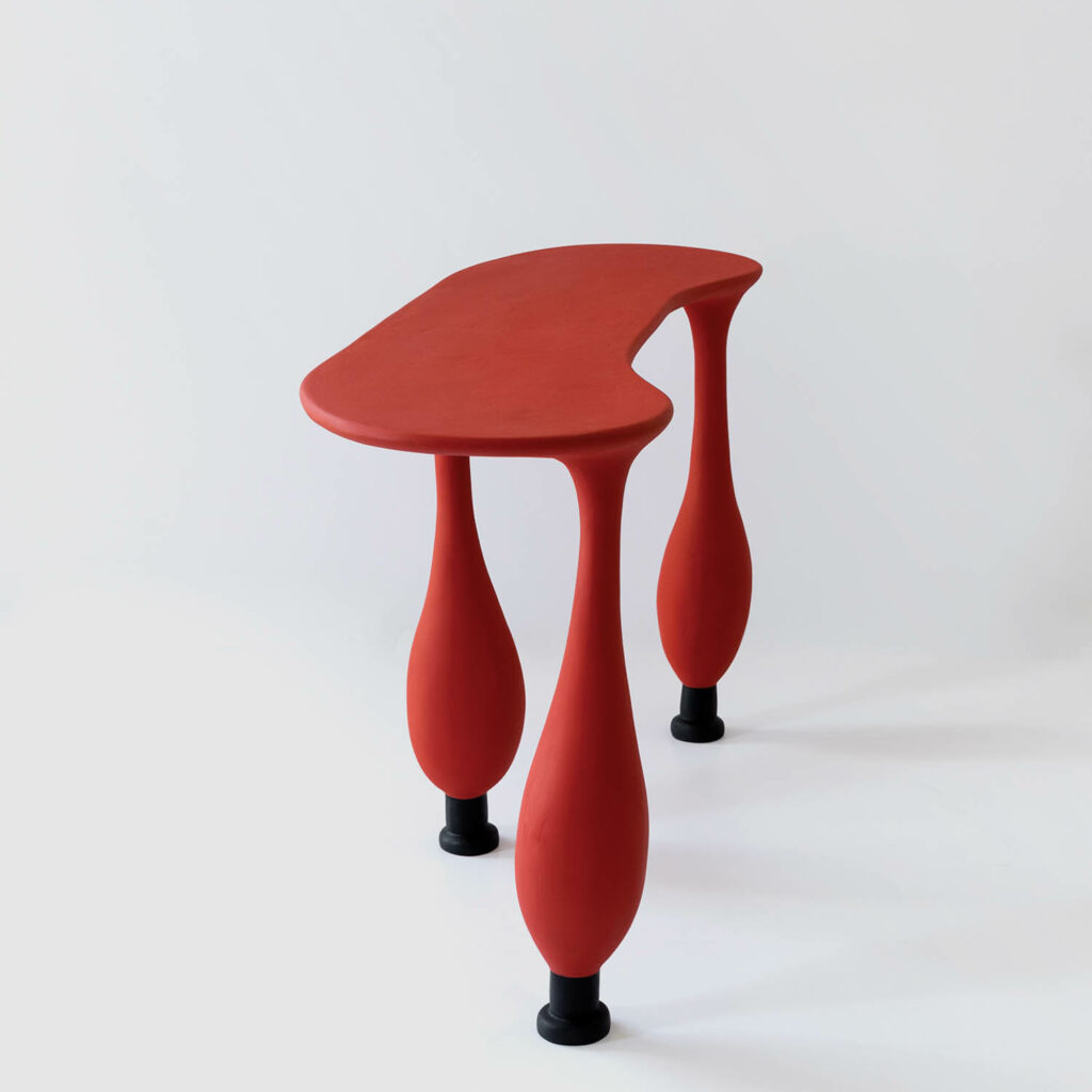 a narrow red table with three bulbous legs
