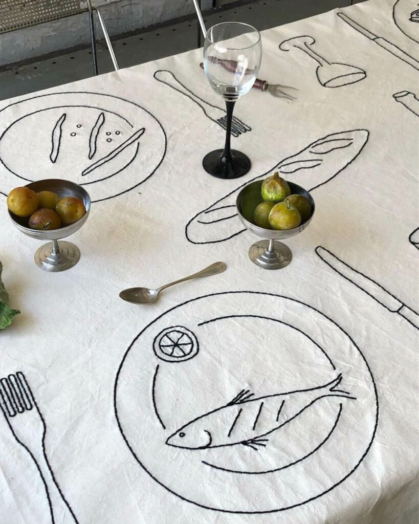 a white tablecloth embroidered with black stitchings of plates and food items