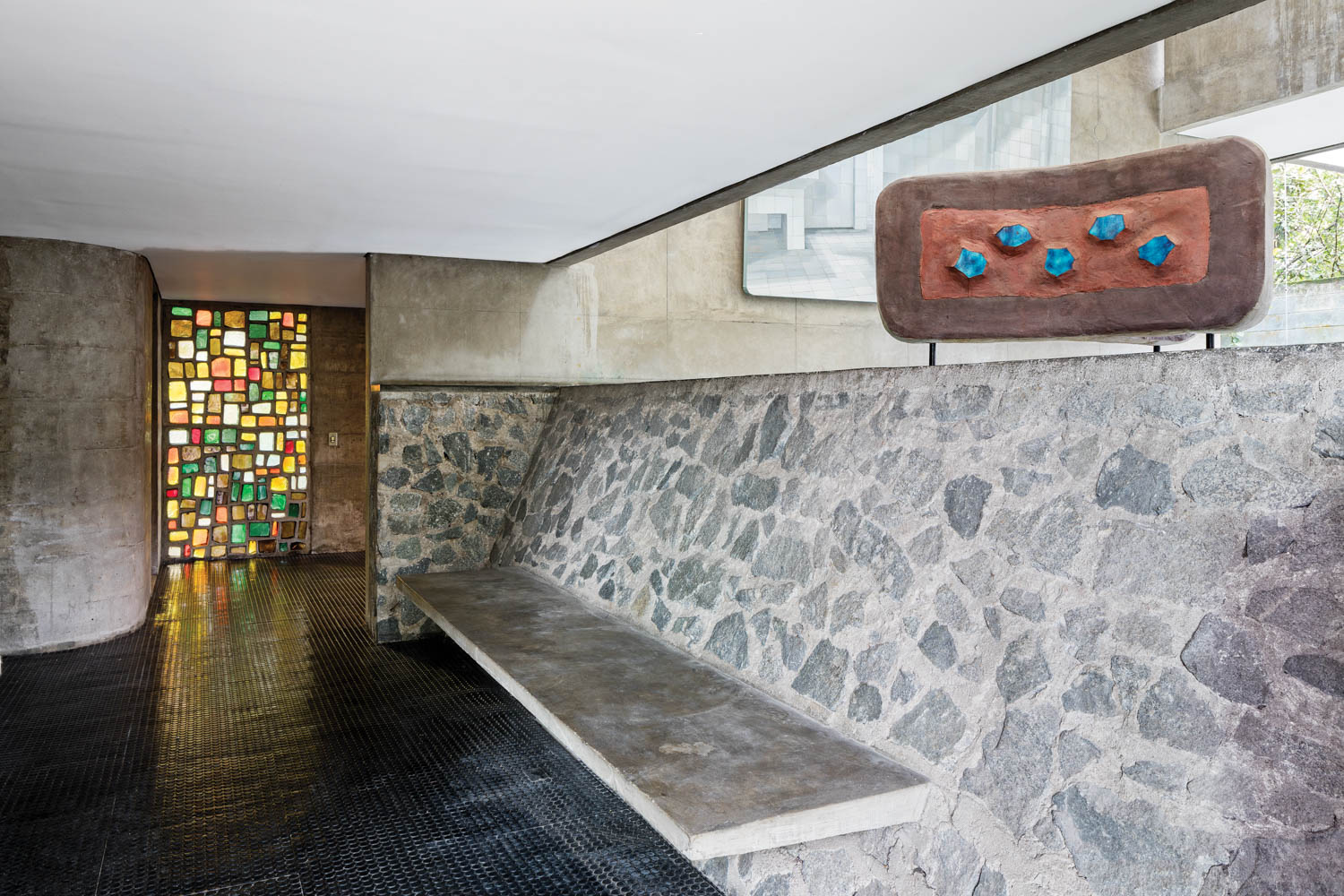 a sculpture overlooks a stone wall and a stained glass window is in the forefront