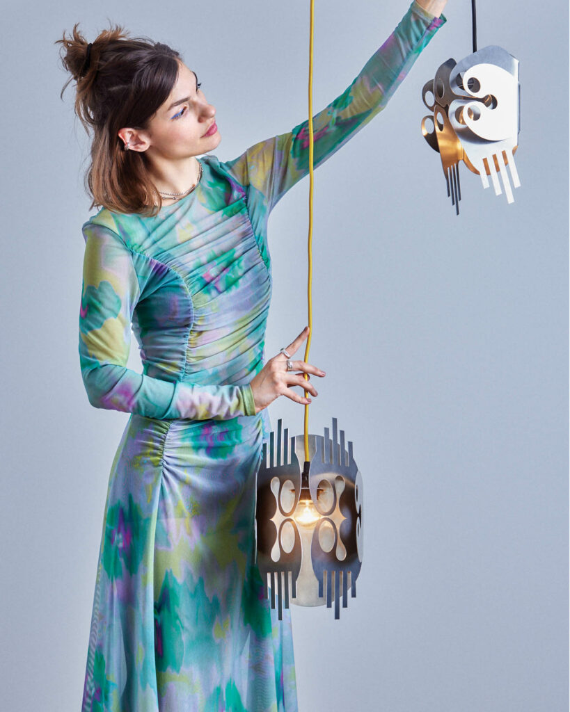 a woman in a teal dress holds sculptural lighting
