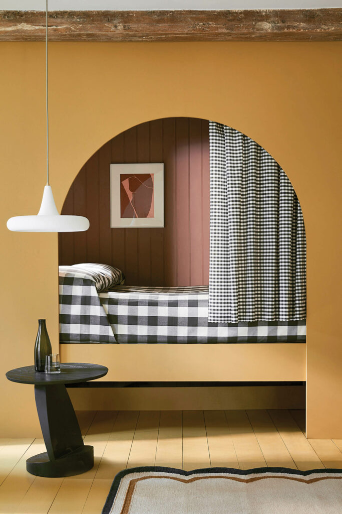 a saffron wall with a curved mirror and hanging pendant