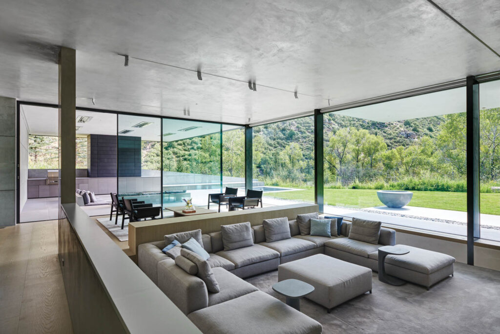 a living room with glass walls looking out to a forest