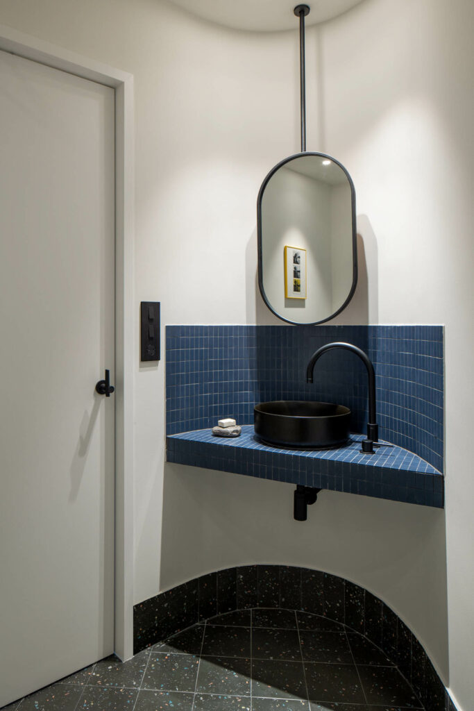 A corner sink in blue tile with an oval mirror