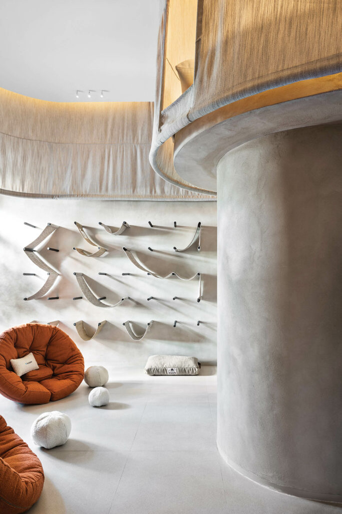 a wall of cat hammocks in a gray room with a large column and orange chair