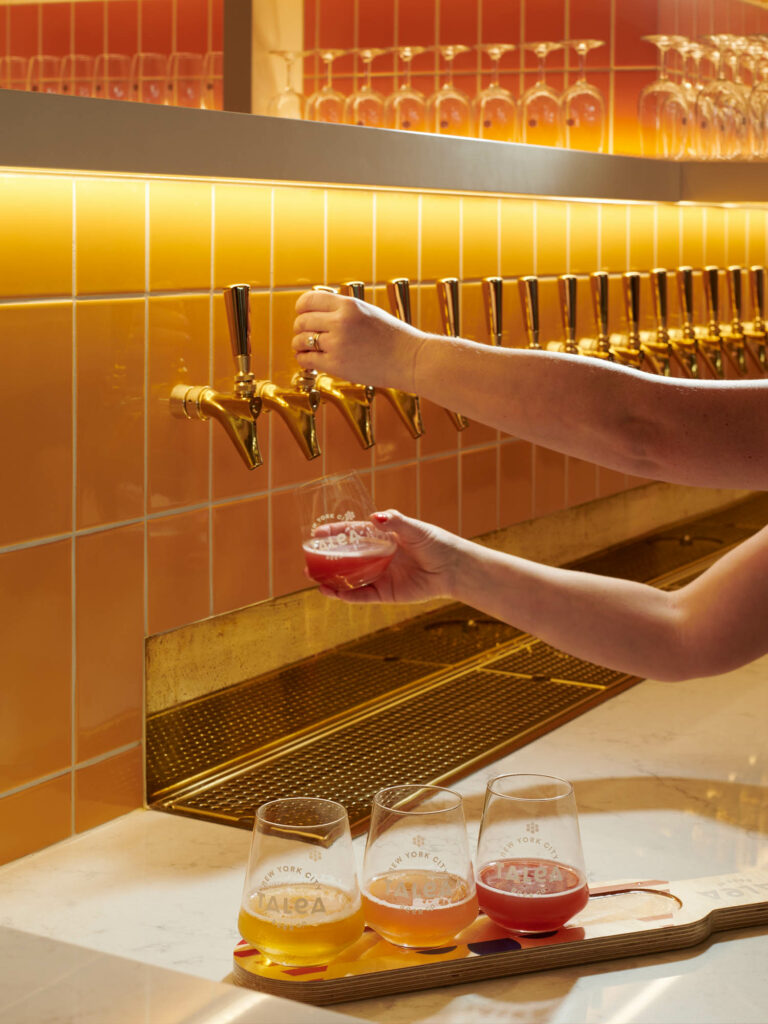 a person pouring beer from a tap along a yellow tiled wall