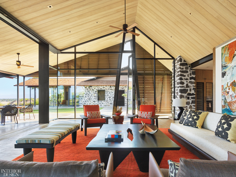 A pitched wooden ceiling balances the vibrant furnishings below including a striped bench and an orange rug and armchairs